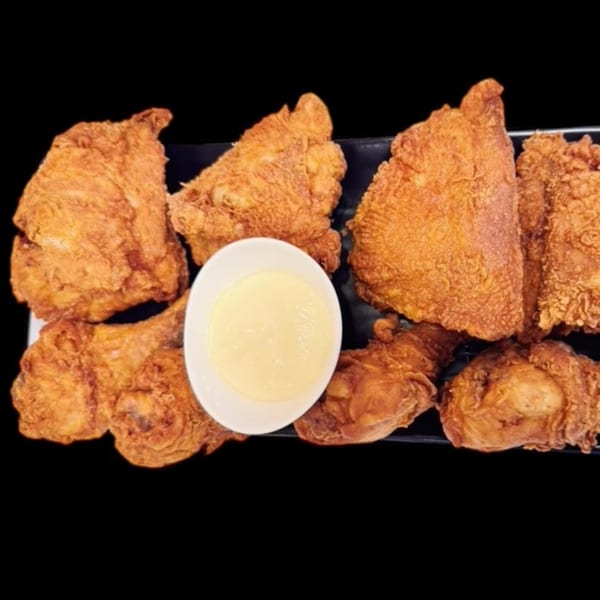 Crispy fried chicken pieces and drumsticks with a side of creamy white dipping sauce.