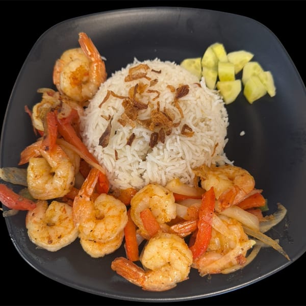 Shrimp with red peppers and onions, served with white rice topped with fried onions and cucumber slices.