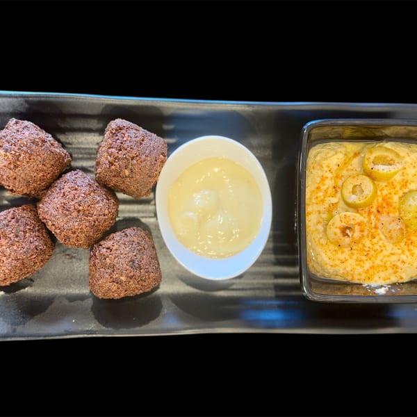 Five brown falafel balls, a white bowl of tahini, and a rectangular dish of hummus with olives.