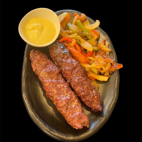 Sharjah Mediterranean Grill's kofta kebabs with sautéed bell peppers and onions, served with a side of sauce.